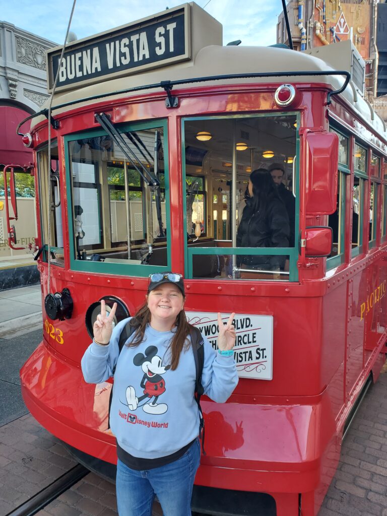 woman standing in front of red trolley at disney california adventure wearing blue mickey mouse sweatshirt